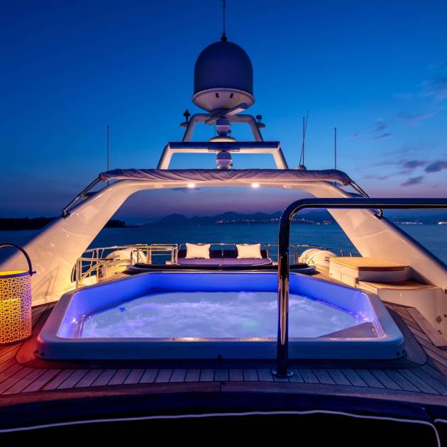 A luxury yacht with lights and a jacuzzi sailing in the sea at night